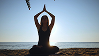 Silhouette of beautiful young woman practicing morning yoga in lotus pose on tropical sea beach with tree palms