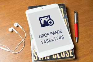 White tablet mockup of an Apple iPad on a book beside a pen and earphones on a wooden table